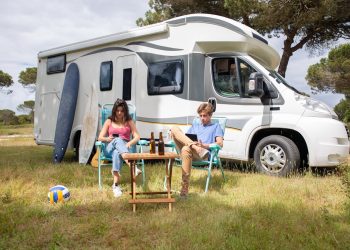 A couple enjoys a sunny day relaxing by their camper van in a picturesque outdoor setting in Portugal.